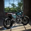 motocicleta scrambler de culoare verde fotografiata intr-o incapere langa o fereastra