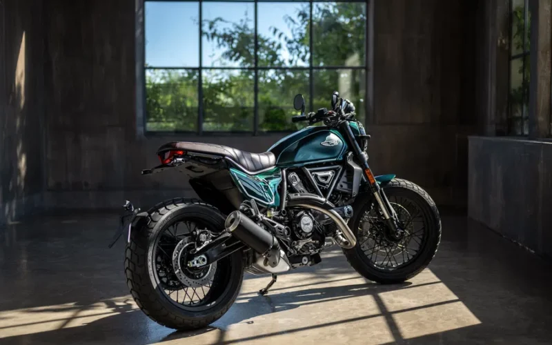 motocicleta scrambler de culoare verde fotografiata intr-o incapere langa o fereastra