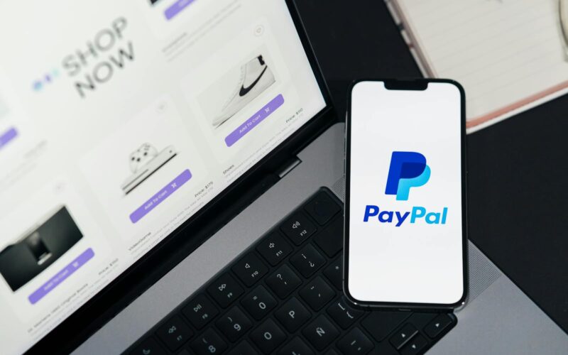 Smartphone cu logo-ul Paypal langa un laptop deschis pe un site de cumparaturi