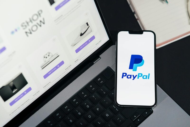 Smartphone cu logo-ul Paypal langa un laptop deschis pe un site de cumparaturi