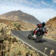 motocicleta adventure rosie pe drum virajat inclinata pe partea dreapta