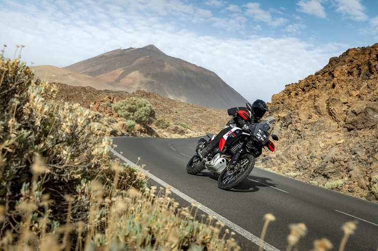 motocicleta adventure rosie pe drum virajat inclinata pe partea dreapta