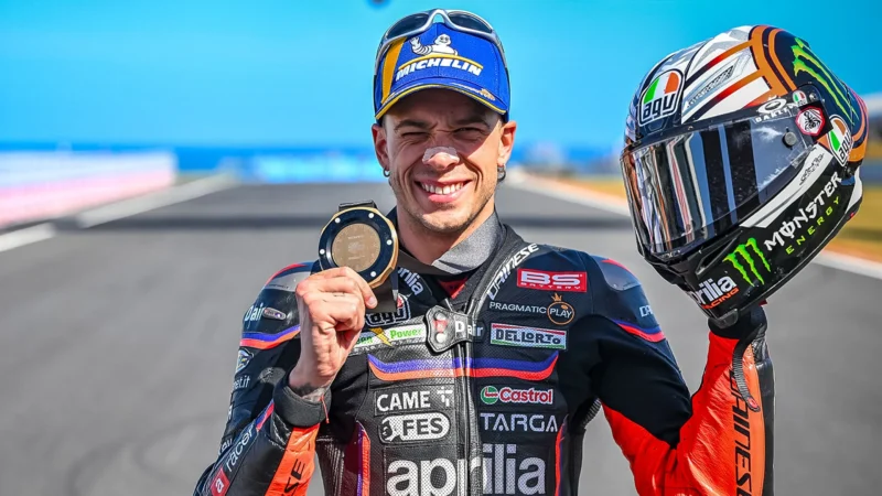 pilot motogp cu casca in mana pe pista de cirucit cu medalia in mana