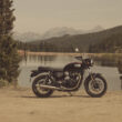 motocicleta clasica de culoare neagra la marginea unui lac montan