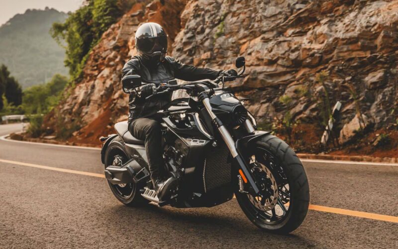 motociclceta de tip cruiser de culoare neagra surprinsa pe un drum de munte cu stanci in fundal