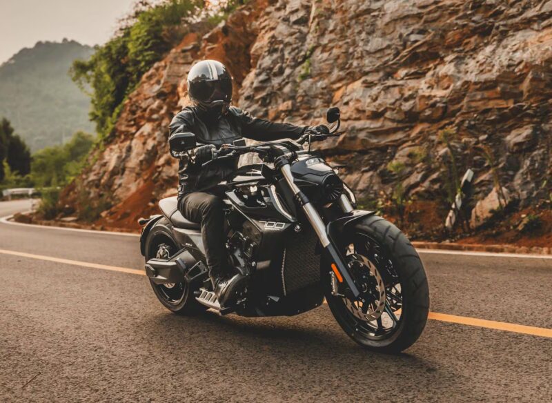 motociclceta de tip cruiser de culoare neagra surprinsa pe un drum de munte cu stanci in fundal