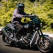 motocicleta cruiser de culoare negra fotografiata pe strada cu o padure in spate