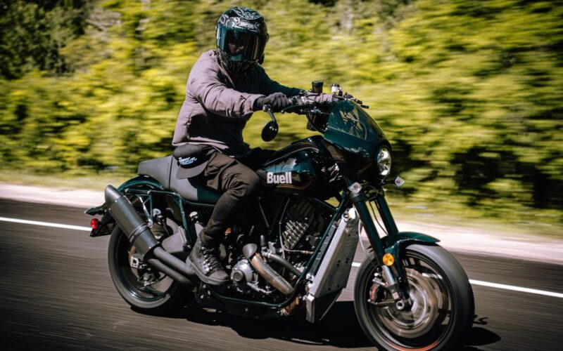 motocicleta cruiser de culoare negra fotografiata pe strada cu o padure in spate