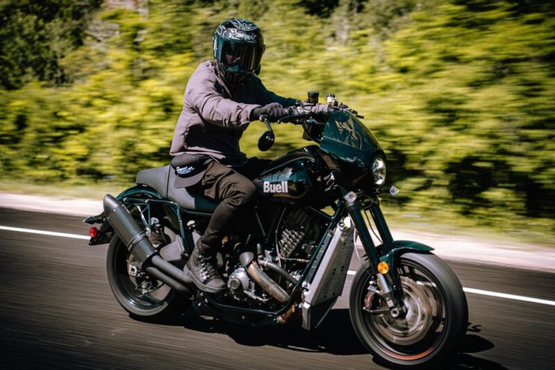motocicleta cruiser de culoare negra fotografiata pe strada cu o padure in spate