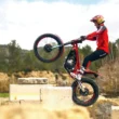 motocicleta trial de culoare rosie executand un tric pe niste blocuri de piatra