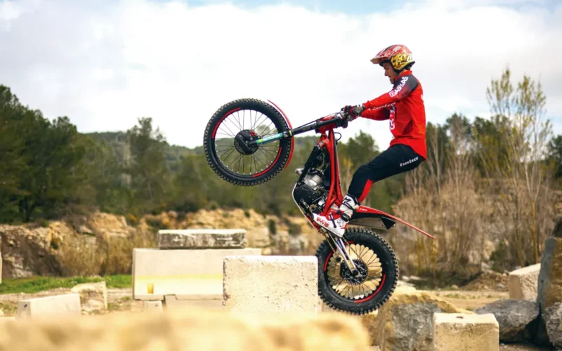 motocicleta trial de culoare rosie executand un tric pe niste blocuri de piatra