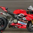 motocicleta rosie de la ducati pe stand in fata unei boxe metalice