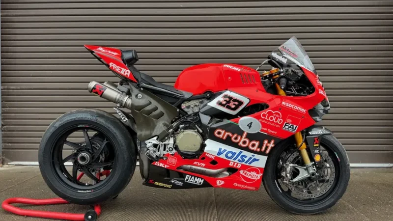 motocicleta rosie de la ducati pe stand in fata unei boxe metalice