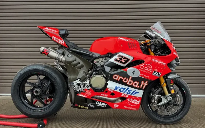 motocicleta rosie de la ducati pe stand in fata unei boxe metalice