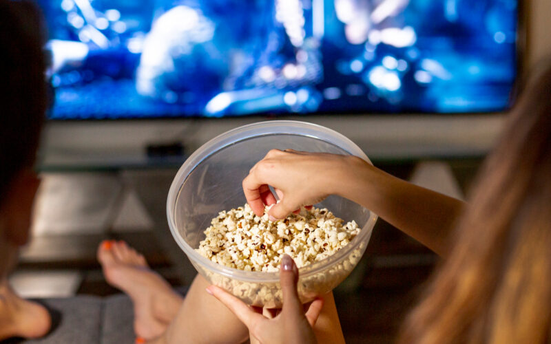 doi oameni mananca floricele in timp ce se uita la televizor