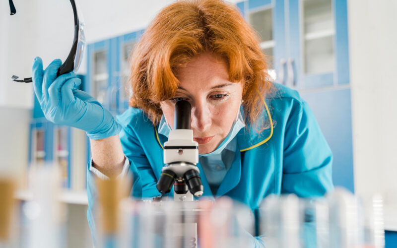 o cercetatoare foloseste un microscop intr-un laborator