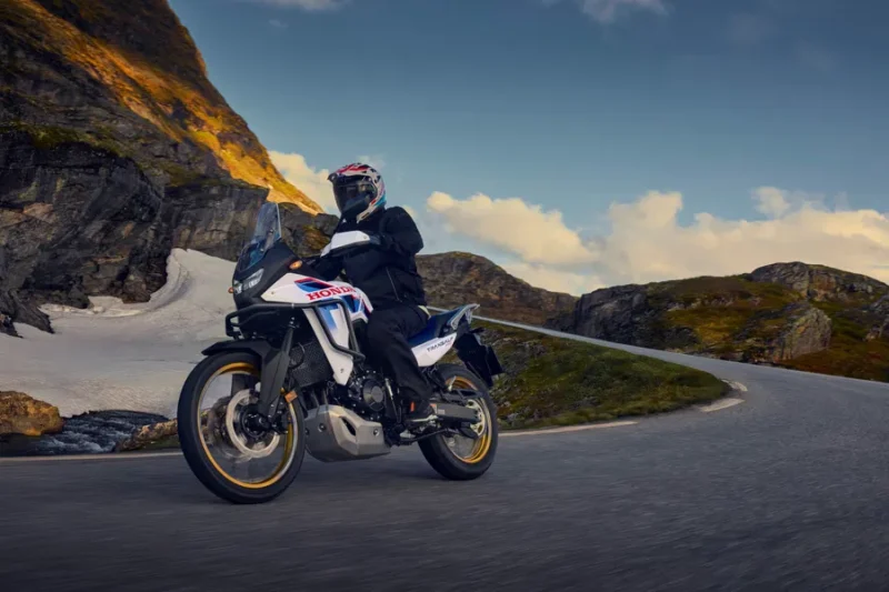 motocicleta honda andventure de culoare alb albastra pe un drum virajat cu un munte in fundal