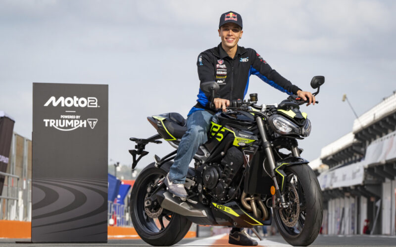 motocicleta naked triumph de culoare neagra cu rider la boxele de pe circuit