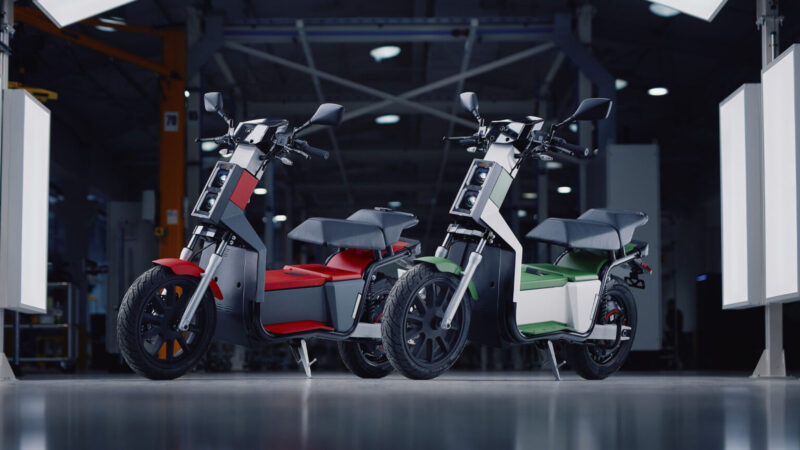 doua scutere electrice unul alb si unul rosu intr-o sala de prezentare
