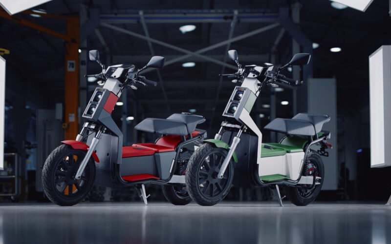 doua scutere electrice unul alb si unul rosu intr-o sala de prezentare
