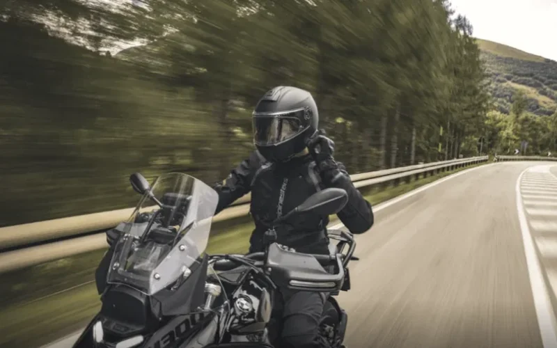 motociclist pe motoreta imbracat in negru cu dealuri in fundal