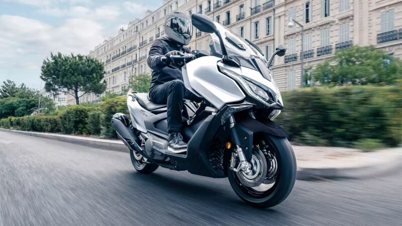 maxi scuter alb cu o cladire in spate