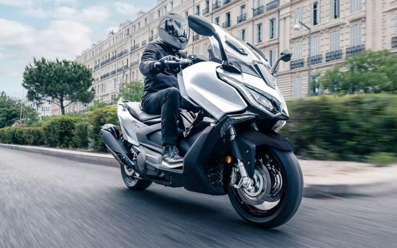 maxi scuter alb cu o cladire in spate