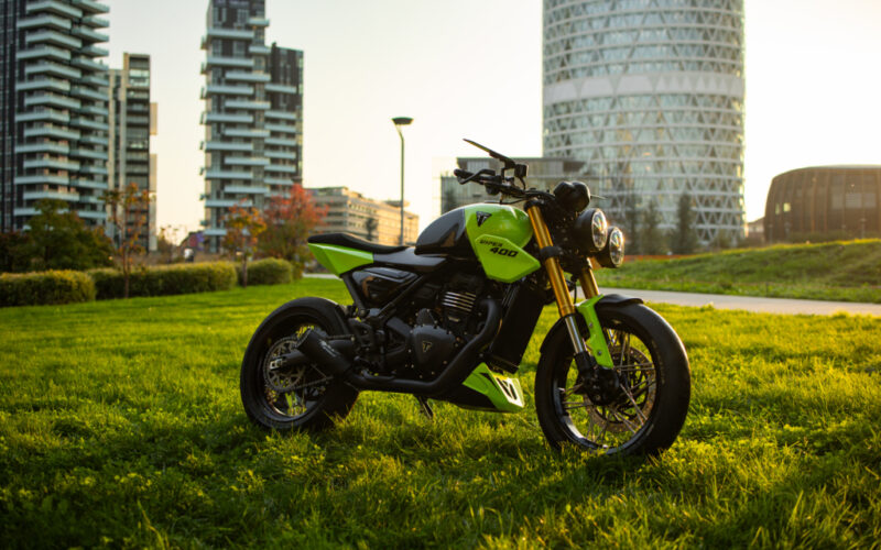 motocicleta verde de tipul naked pe un camp cu cladiri in spate