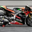 monopost aprilia de culoare negru pe standere in fata unui zid