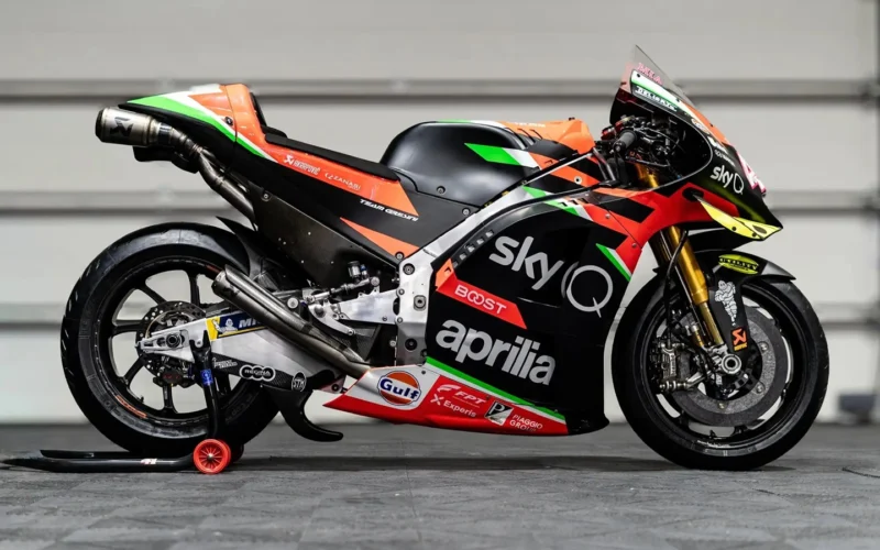 monopost aprilia de culoare negru pe standere in fata unui zid