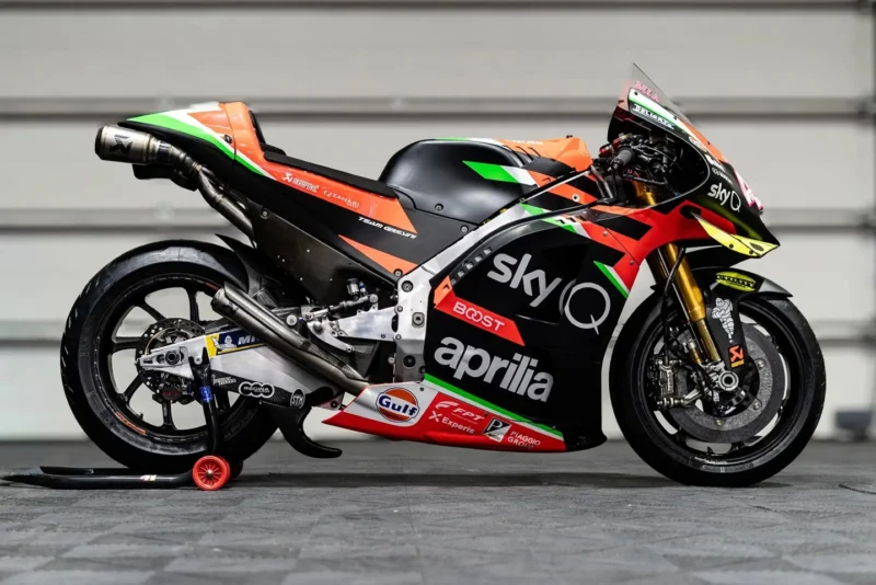 monopost aprilia de culoare negru pe standere in fata unui zid
